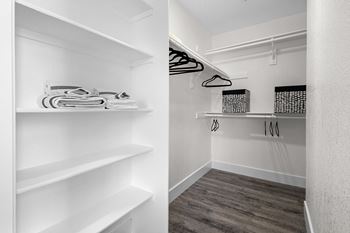 a walk in closet with white shelves and white walls and wood flooring